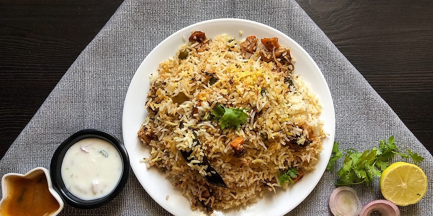 A delicious view of a plate served with biryani and chicken piece sitting on a table.