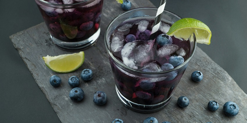 A pair of rock glasses filled with dark liquid, surrounded by fresh blackberries.