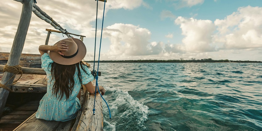 A woman enjoys sailing on a wooden boat, surrounded by calm waters and a clear sky.