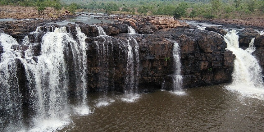 A picture of a waterfall slowly cascading down a hill with small ponds around