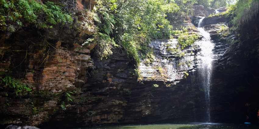 A picture of a landscape with water falling from the rocks at a hill into a pond at the base