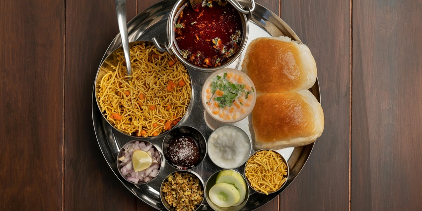 Image of a pav bhaji food platter with colourful dishes a glass of lassi, mixture, onion and lemon on the side