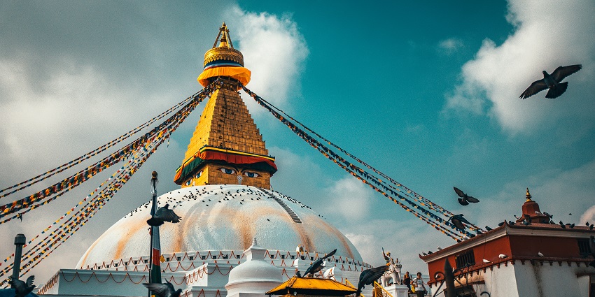 A majestic Buddhist monument, surrounded by prayer flags and bustling activity.