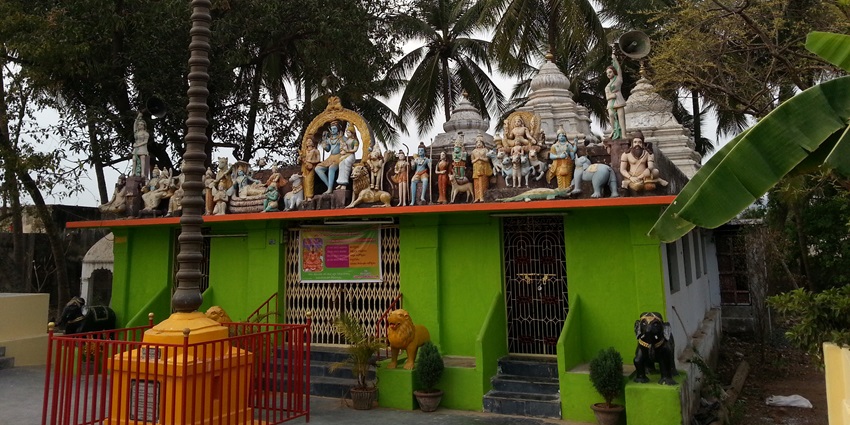 A picture of a traditional temple with colourful walls, surrounded by trees and greenery