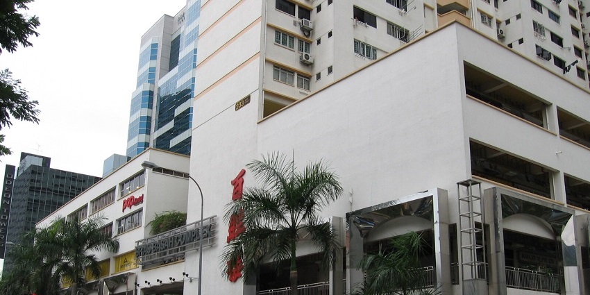 A glimpse of the Bras Basah Complex featuring white buildings, clean roads, and cars.