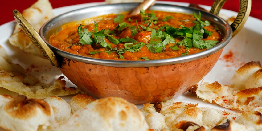 Image of a bowl of soup served with a slice of bread on a wooden table.