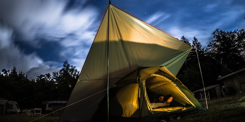 A tent illuminated at night on a hilltop, surrounded by trees and mountains, similar to the best camp in Tosh.