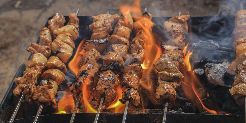 A picture of an outdoor grill with various food items being cooked on the skewers