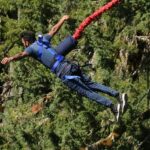 An exhilarating view of a man harnessed with rope jumping off a cliff during the day.