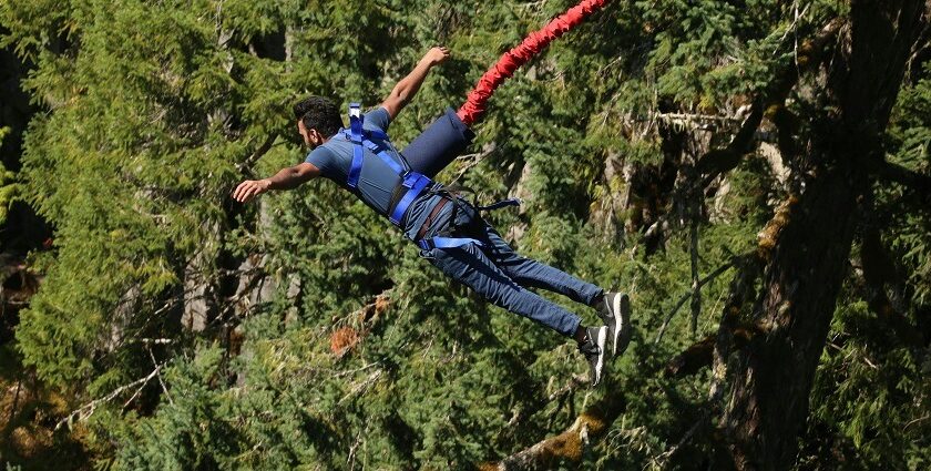 An exhilarating view of a man harnessed with rope jumping off a cliff during the day.