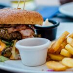 A glimpse of a giant burger filled with chicken and veggies and served with fries.