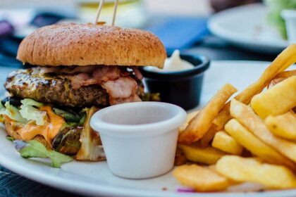 A glimpse of a giant burger filled with chicken and veggies and served with fries.