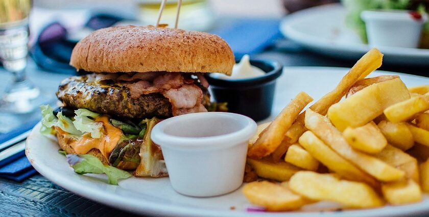 A glimpse of a giant burger filled with chicken and veggies and served with fries.