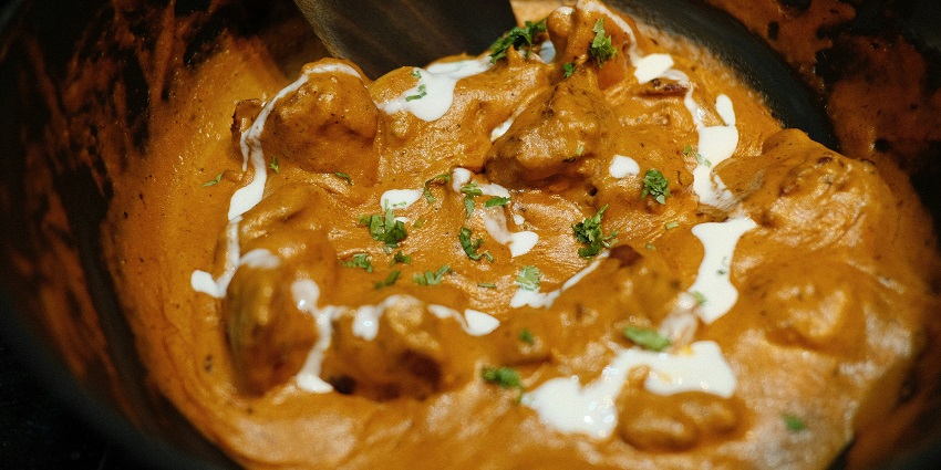 Close up image of butter chicken in a bowl with butter on top - best food in Delhi