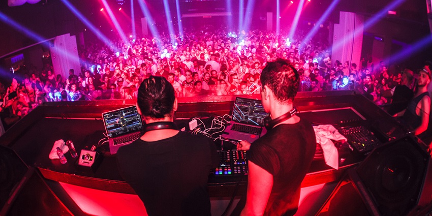 A picture at a nightclub with a live DJ performance in front of the crowd
