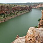 Body of water nestled between rocky cliffs with a clear blue sky - Camping in Gandikota