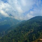 A scenic valley with lush greenery, framed by towering mountains under a bright blue sky