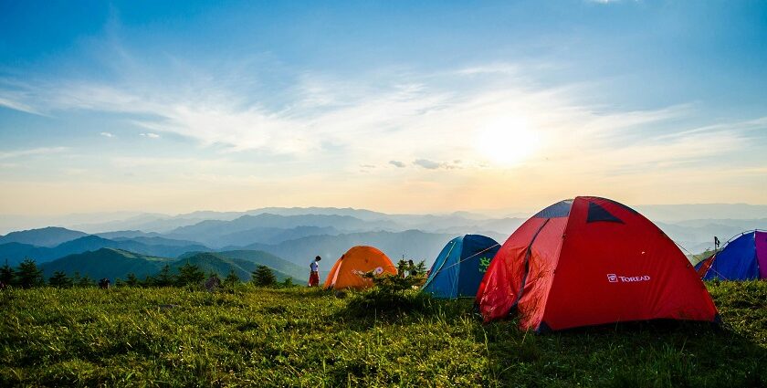 A breathtaking view of dome-shaped camps on a lush green mountain range during the day.