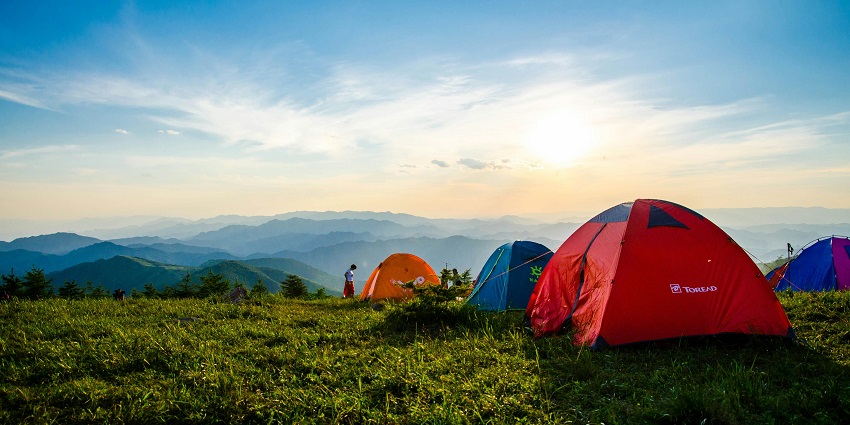 A breathtaking view of a lot of colourful camps on a lush green mountain in the day.
