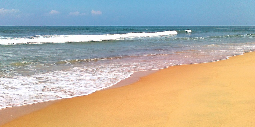 A picture of a beach with a vast coastline and sheet of blue waters in front