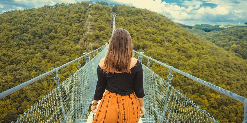 Image of a woman walking on a suspended canopy walkway surrounded by lush trees.