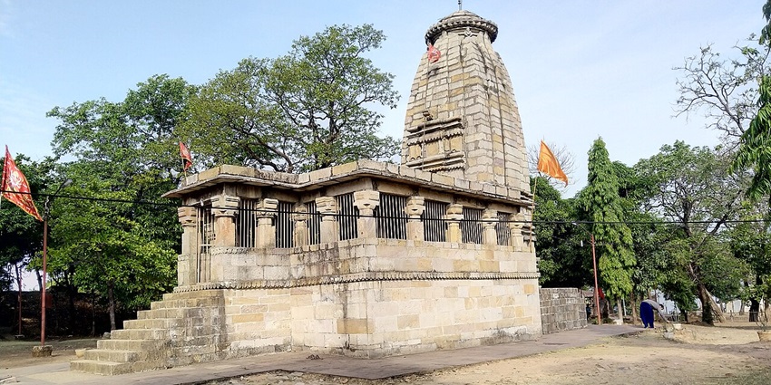 Ancient stone temple with intricate carvings, set amidst a lush green landscape.