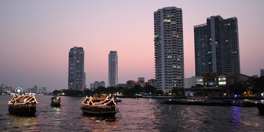 Boats floating in the Chao Phraya river in the evening and buildings in the background