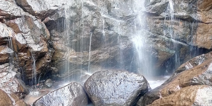 A picture of a waterfall cascading down a rocky hill with a pond of water in front of the fall