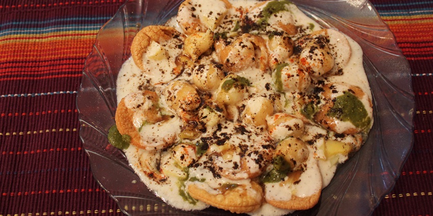 Gujarati street food dish topped with curd, chutneys, spices, and crispy fried snacks.