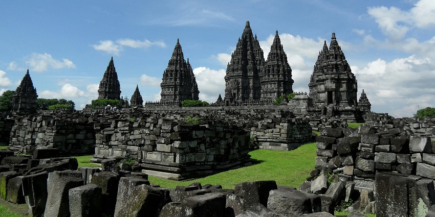 A stone temple stands tall under a blue sky with scattered white clouds, creating a sense of space and contrast against the open sky.