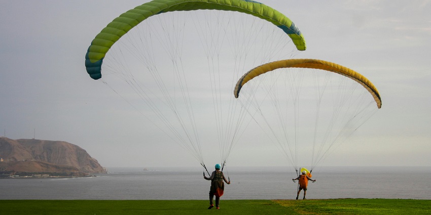 People with parachutes gently land on a sandy seashore, concluding their skydiving.