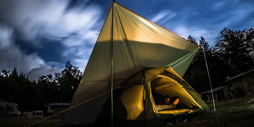 A tent pitched on a grassy hilltop overlooking a vast, scenic valley under a clear blue sky.