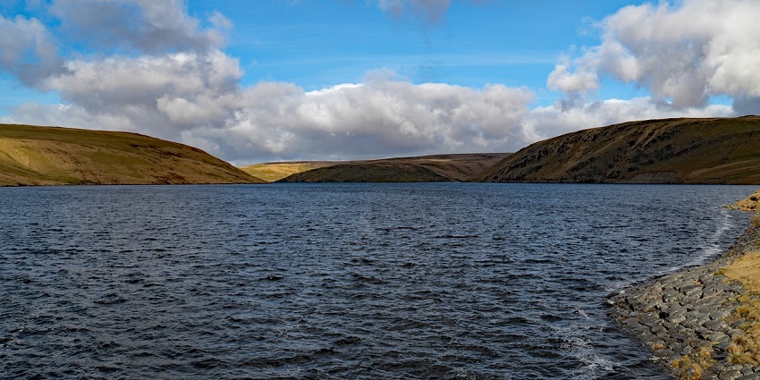 A panoramic view of a water reservoir, surrounded by rugged terrain and natural greenery.