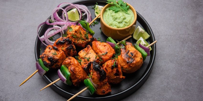 Chicken tikka served with three different chutneys and lemon, plated with creativity