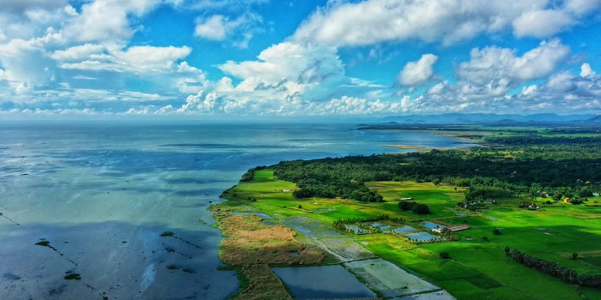 A mesmerising view of the Chilika Lake with lush greenery around it and cloudy skies.