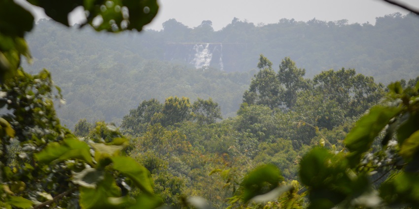 Top view of the waterfall, tall mountains, and greenery from a valley during dawn.