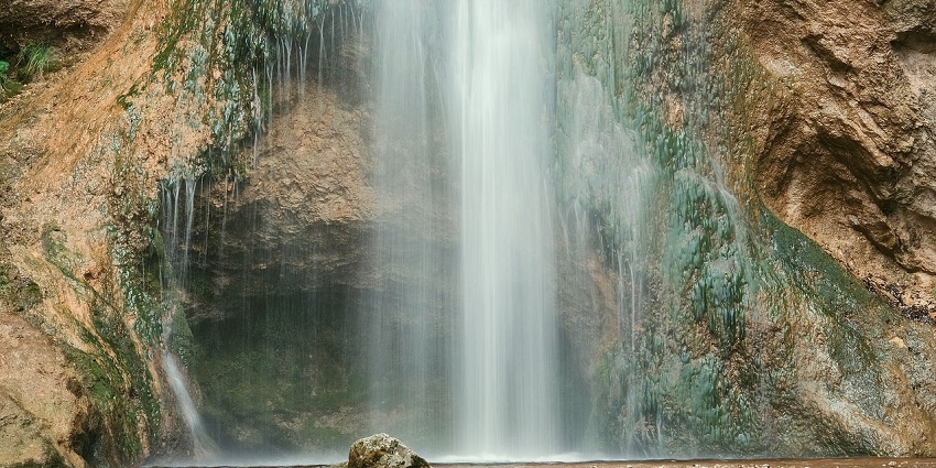 A breathtaking view of the Chimi Waterfalls surrounded by lush green meadows in the day.