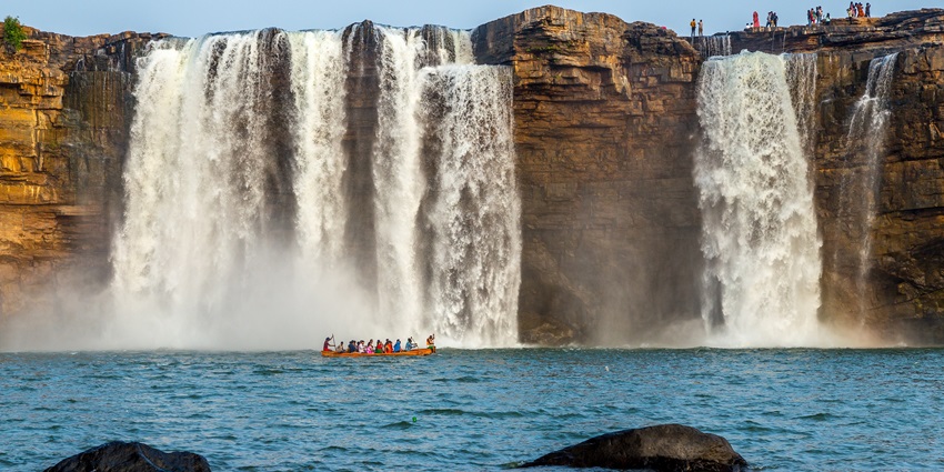 A boat full of people is passing by while the majestic waterfalls are flowing down