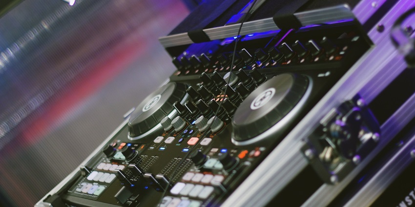 A lively nightclub scene, with people dancing under colourful lights with a DJ console.