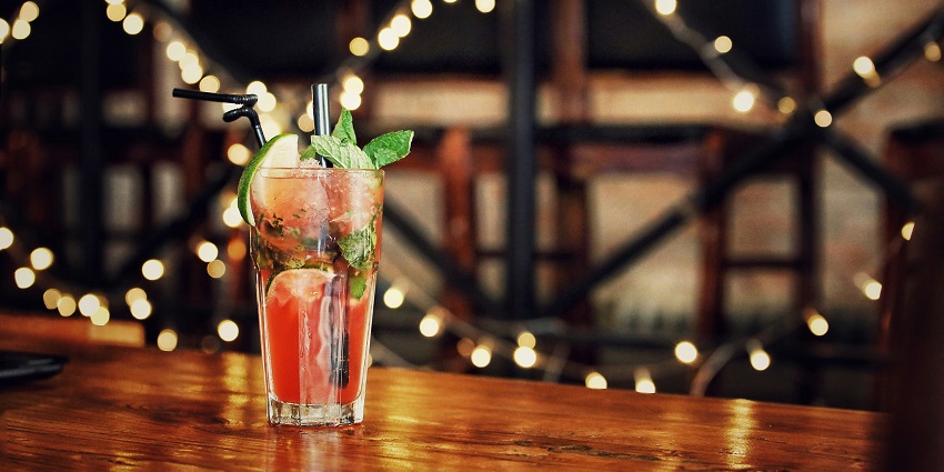 Clear drinking glass sits on a brown wooden surface, reflecting light beautifully.