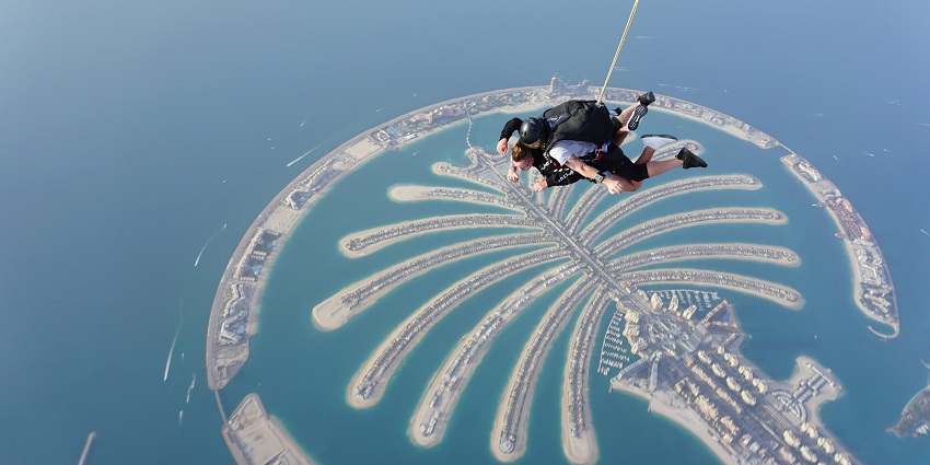 An image fo two people with a yellow and blue-coloured parachute flying in the air.