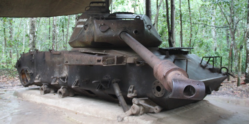 An entry point to the Cu Chi Tunnels in Vietnam, featuring a small, covered hole surrounded by dense green foliage.