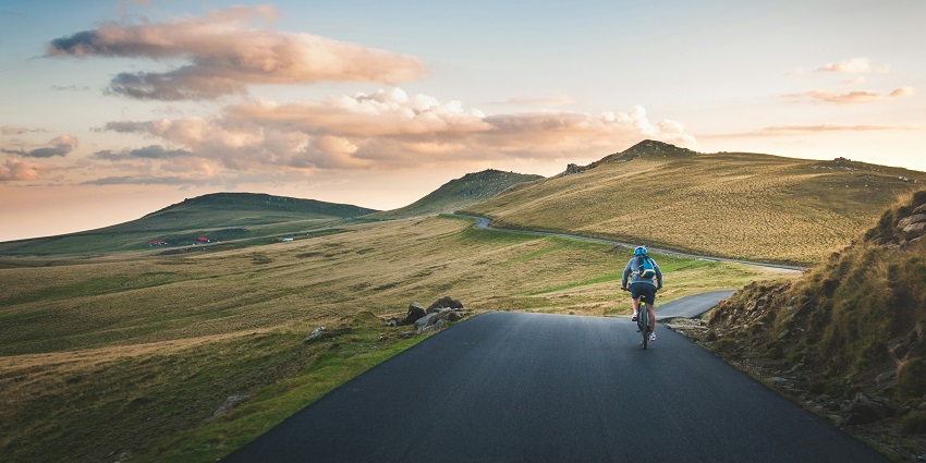 Image of a person cycling around the valleys on twisty road during day time