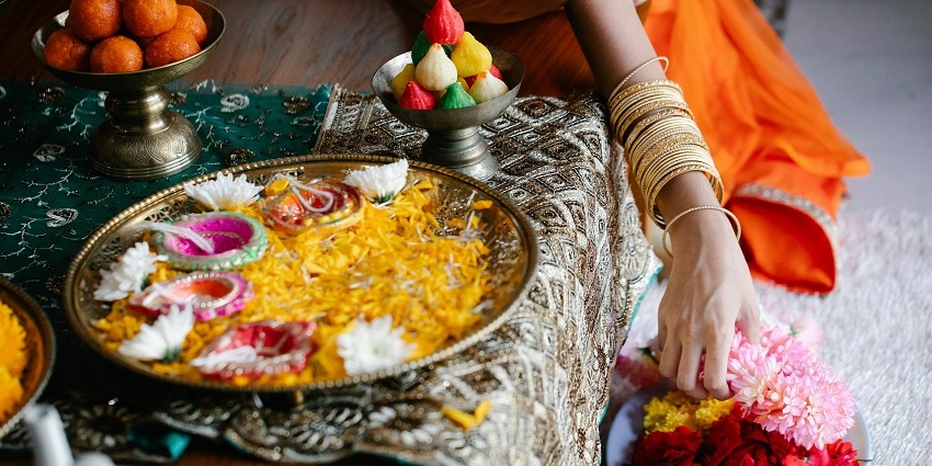 A marvellous view of a pooja thali with lamps and lot of flowers with a woman’s hand.
