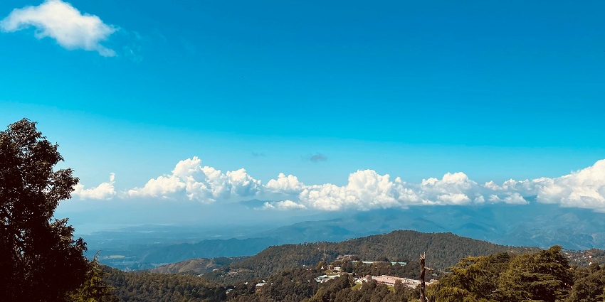 Scenic view of Dalhousie lush green mountains under clear blue sky and clouds