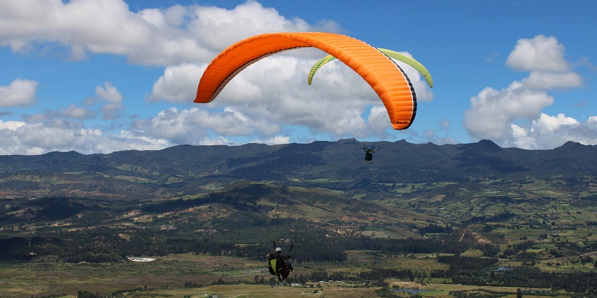 A person paragliding with an orange parachute against a clear blue sky, enjoying the thrill of flight