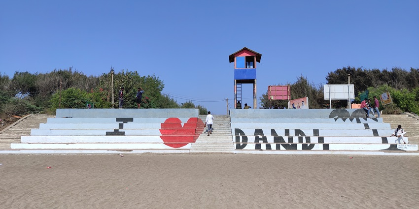 Dandi Beach with calm waves and a few scattered visitors under a clear sky in Gujarat.