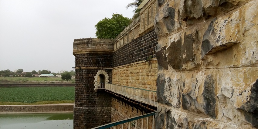Stone walls and detailed carvings adorn Darbargadh Palace, overlooking a serene green moat