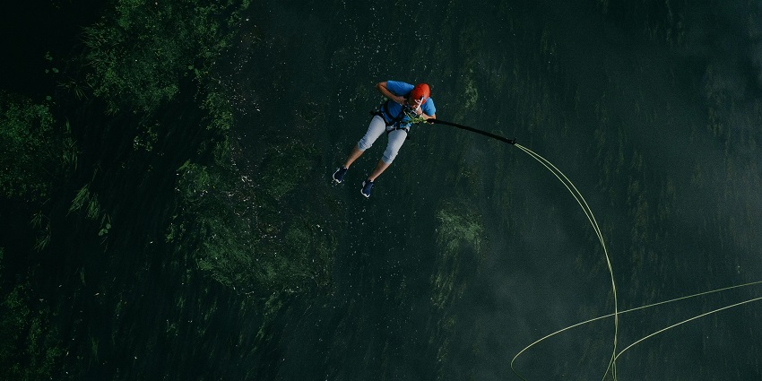 A fantastic view of a man harnessed with ropes taking a jump into the air around greenery.