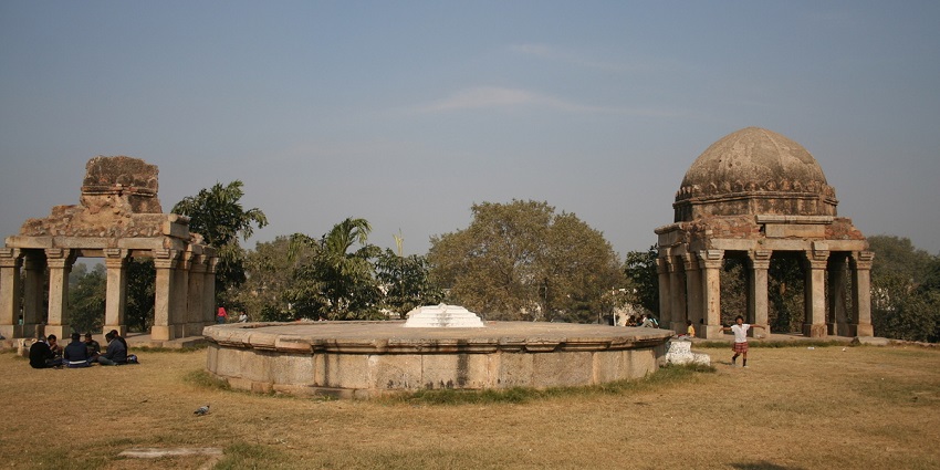 Ancient stone pavilions and a circular platform on a grassy lawn under a clear blue sky.